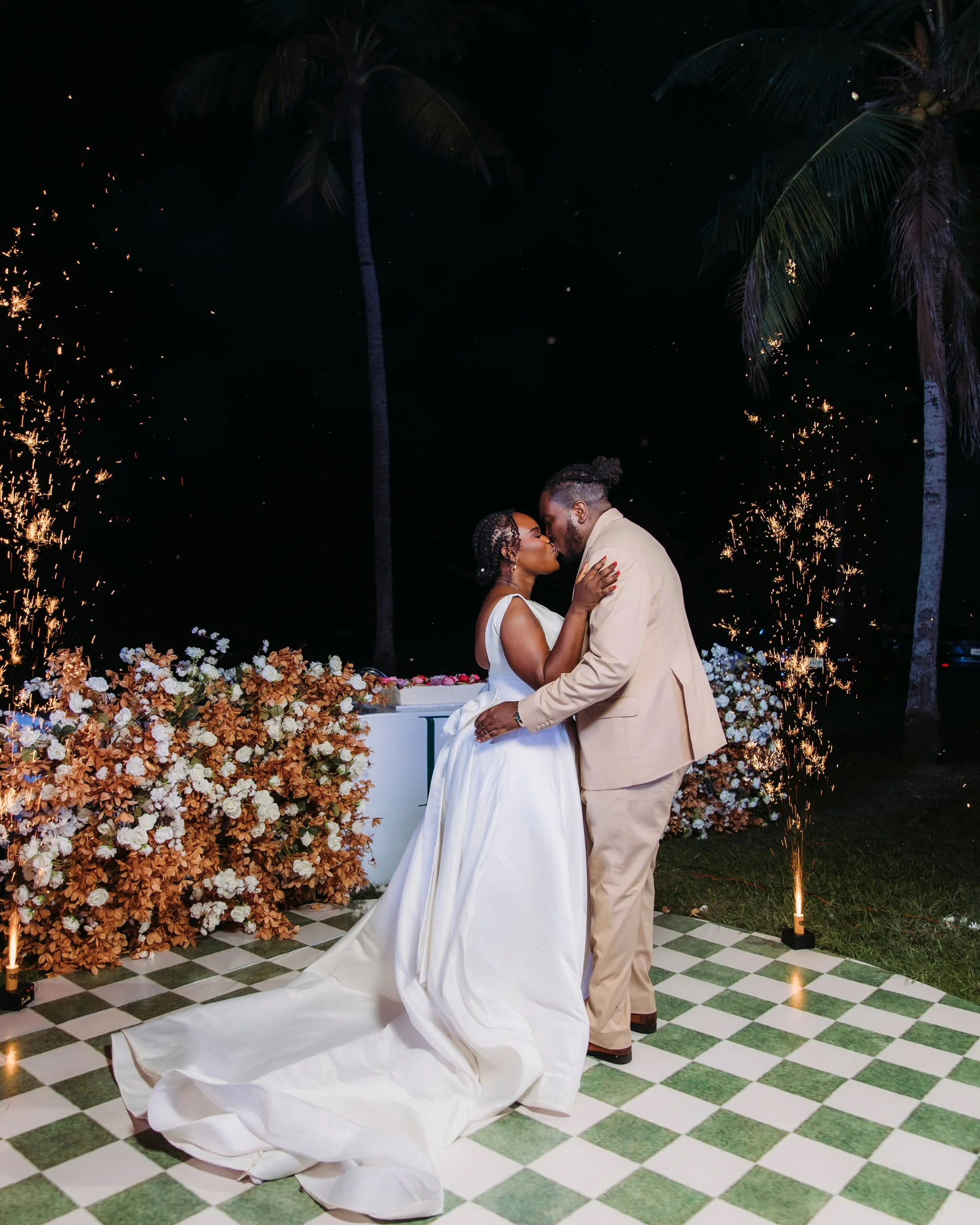 Couple kissing on a checkered dance floor as sparkler fountains light the night