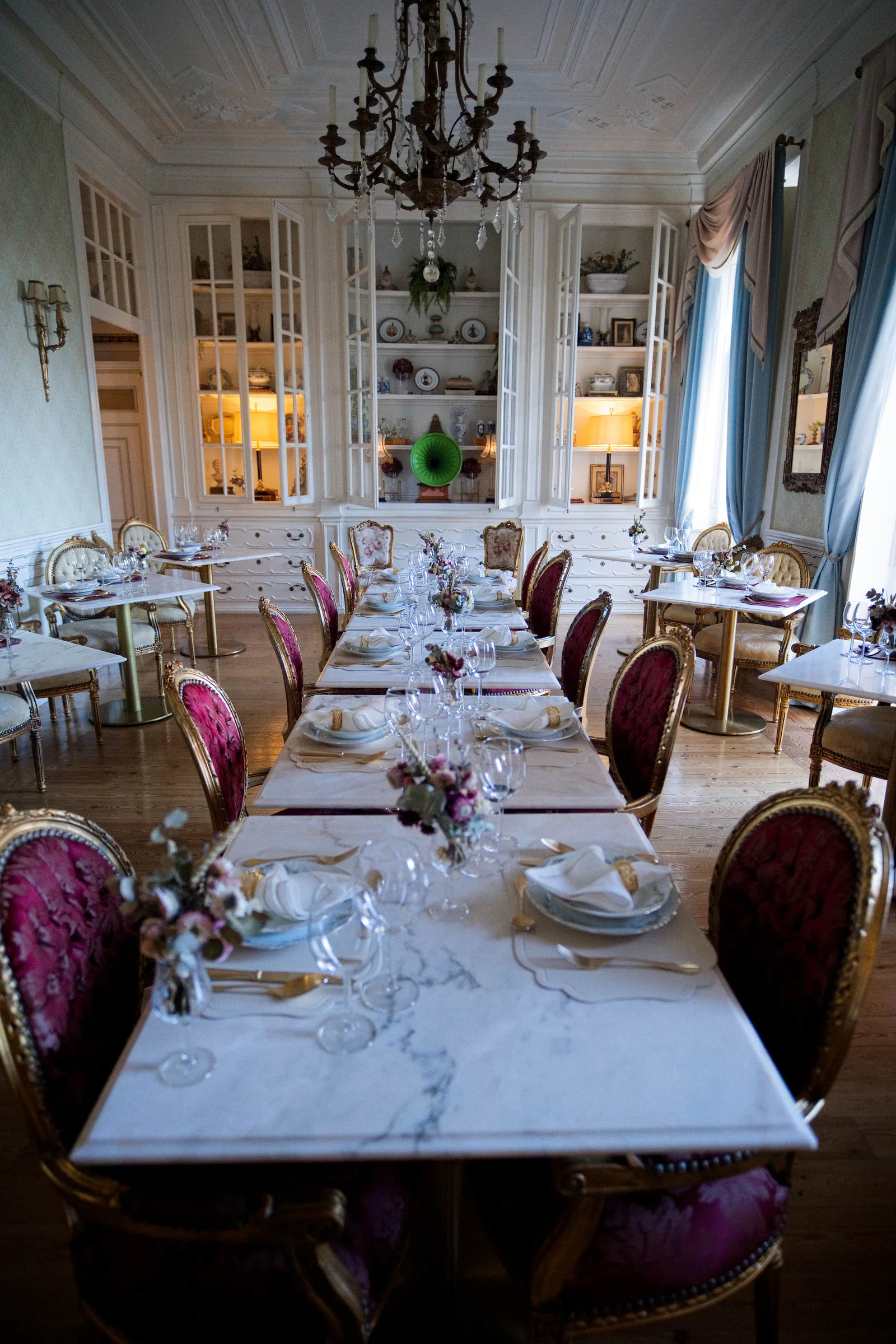 Long marble dining table dressed for dinner in a chandelier-lit palace dining room