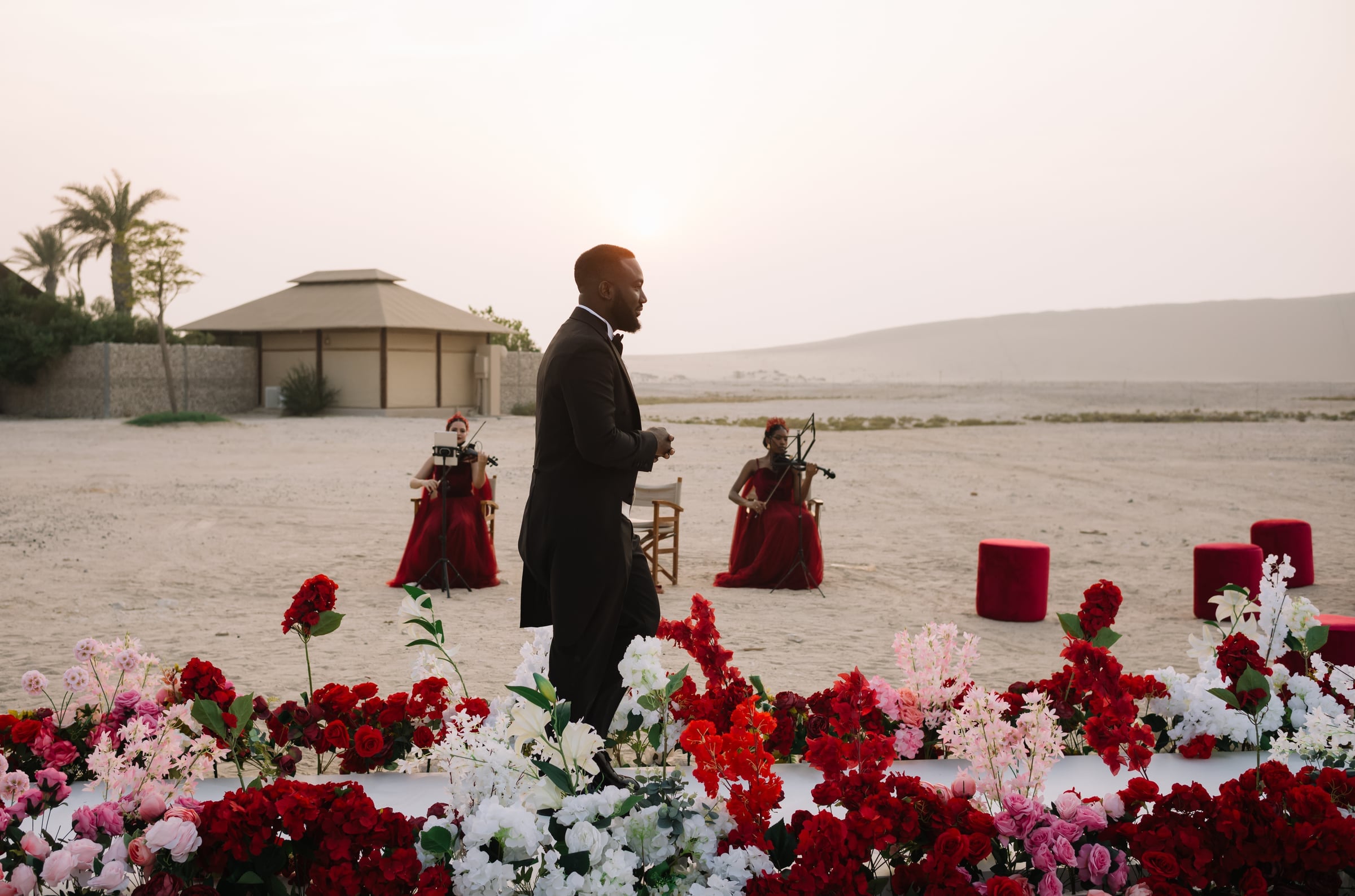 Violinists in red at a desert celebration at sunset, framed by a low wall of roses